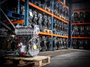 Photo qui montre un moteur Renault Master 3 M9T sur une palette et en arrière plan plusieurs moteurs véhicules exposé sur des racks qui montre le stock de l'entrepôt France Moteurs Utilitaires.