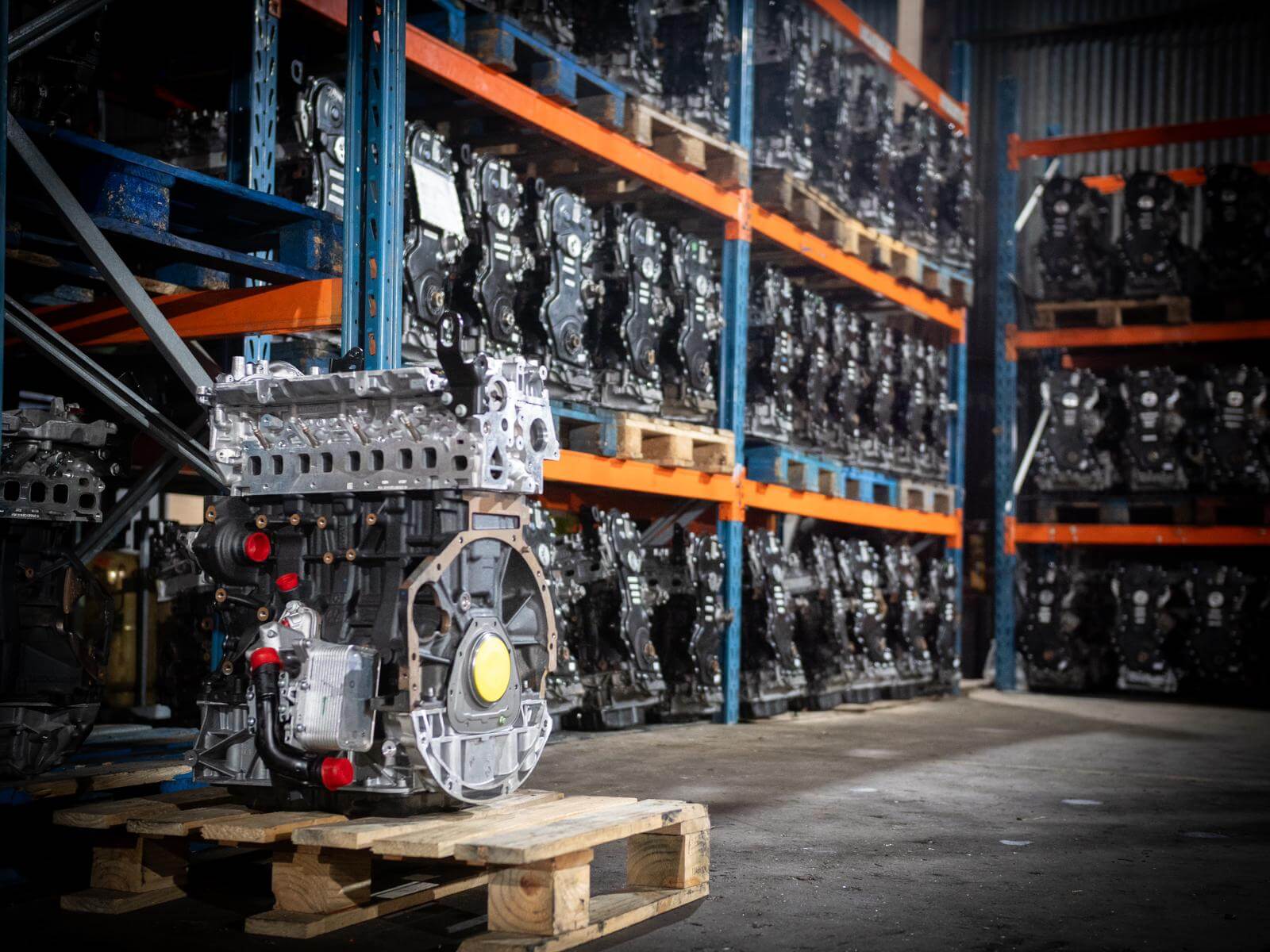 Photo qui montre un moteur Renault Master 3 M9T sur une palette et en arrière plan plusieurs moteurs véhicules exposé sur des racks qui montre le stock de l'entrepôt France Moteurs Utilitaires.